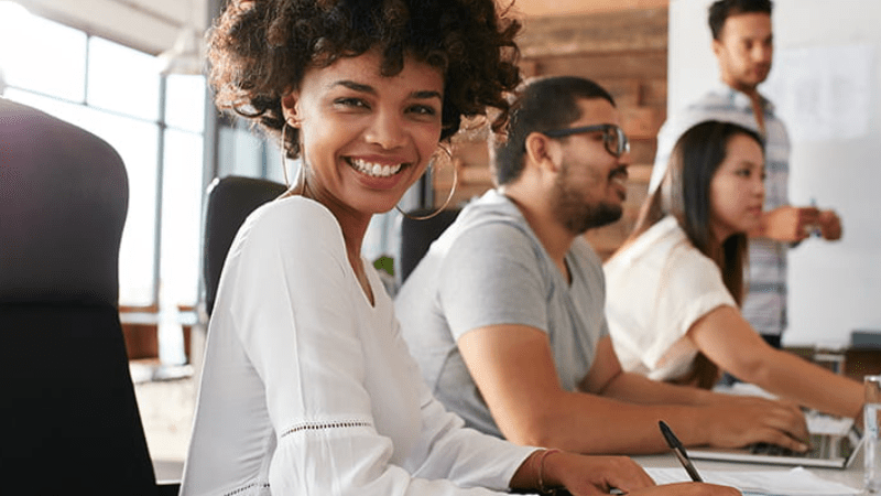 Un groupe de personne travaille et une dame nous regarde en souriant Un groupe de personne travaille et une dame nous regarde en souriant